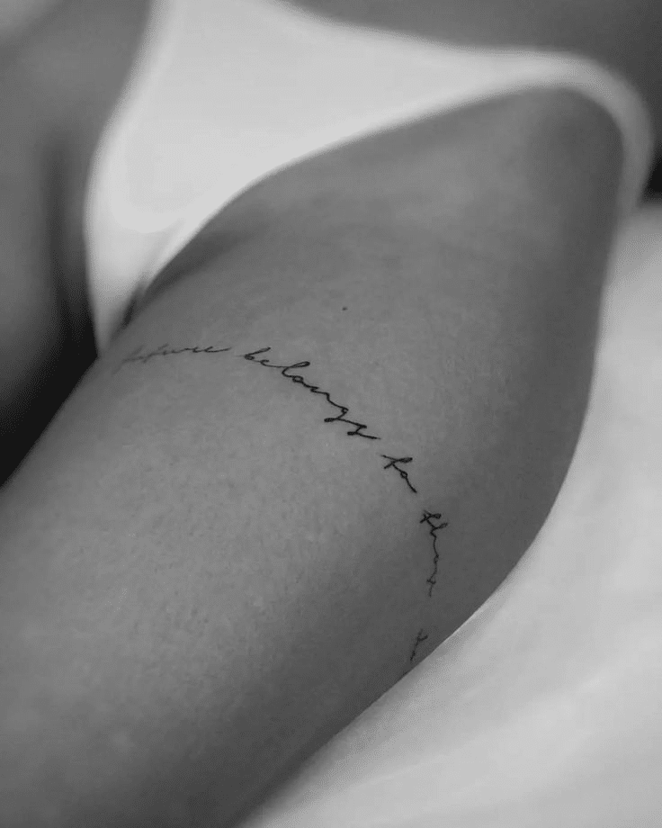 image Minimalist script tattoo on upper thigh in black ink, close-up shot. | Sky Rye Design Minimalist script tattoo on upper thigh in black ink, close-up shot.