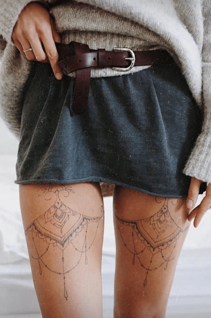 image Woman in a cozy sweater and skirt with intricate thigh tattoos, accented by a brown leather belt, showcasing a boho-chic style. | Sky Rye Design Woman in a cozy sweater and skirt with intricate thigh tattoos, accented by a brown leather belt, showcasing a boho-chic style.