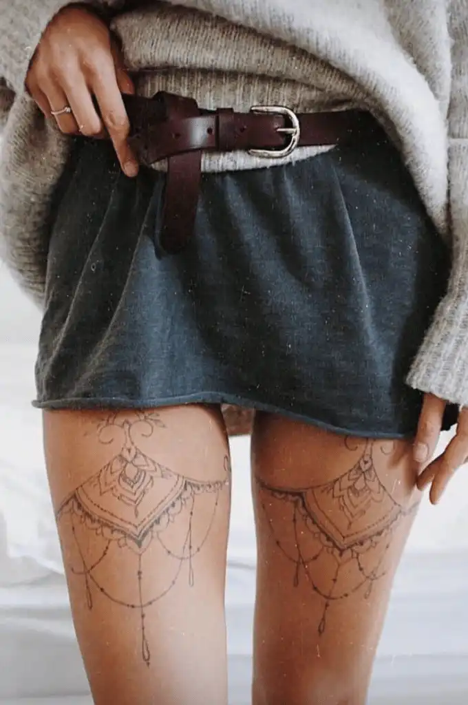 Woman in a cozy sweater and skirt with intricate thigh tattoos, accented by a brown leather belt, showcasing a boho-chic style.