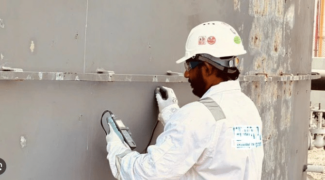 Technician in safety gear uses equipment for industrial inspection on large metal tank. Professional assessment and maintenance work.