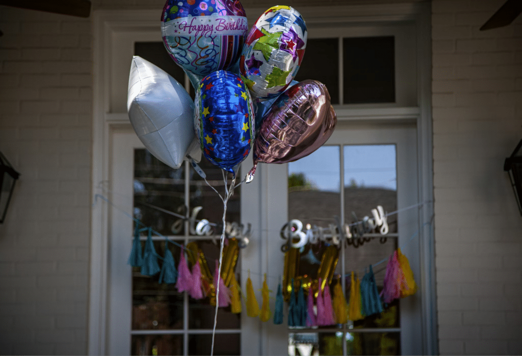Colorful birthday balloons and decorations at a front door celebration, with a Happy Birthday banner and tassel garlands.