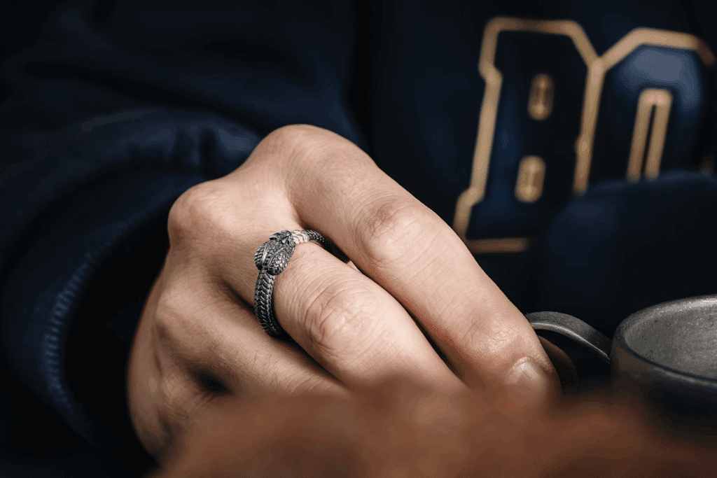 image A hand wearing a detailed snake ring holds a metallic cup against a navy blue background, showcasing intricate jewelry craftsmanship. | Sky Rye Design A hand wearing a detailed snake ring holds a metallic cup against a navy blue background, showcasing intricate jewelry craftsmanship.
