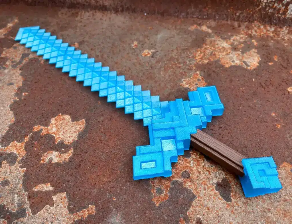 img_4915 Blue pixelated toy sword resembling a Minecraft design, lying on a rusty metal surface, showcasing a unique geometric pattern. | Sky Rye Design Blue pixelated toy sword resembling a Minecraft design, lying on a rusty metal surface, showcasing a unique geometric pattern.