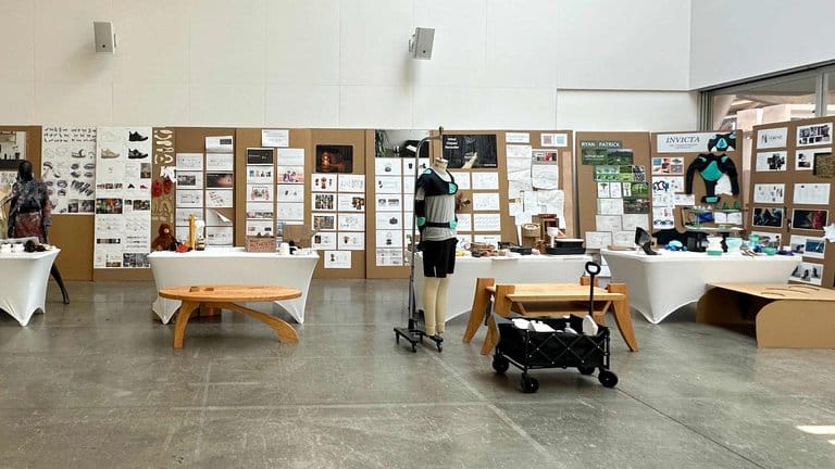 industrial-design-Jr-Review-25-1584-2025-herowidth-768 Exhibition space showcasing design projects with mannequins, presentation boards, and tables displaying various prototypes and artwork. | Sky Rye Design Exhibition space showcasing design projects with mannequins, presentation boards, and tables displaying various prototypes and artwork.