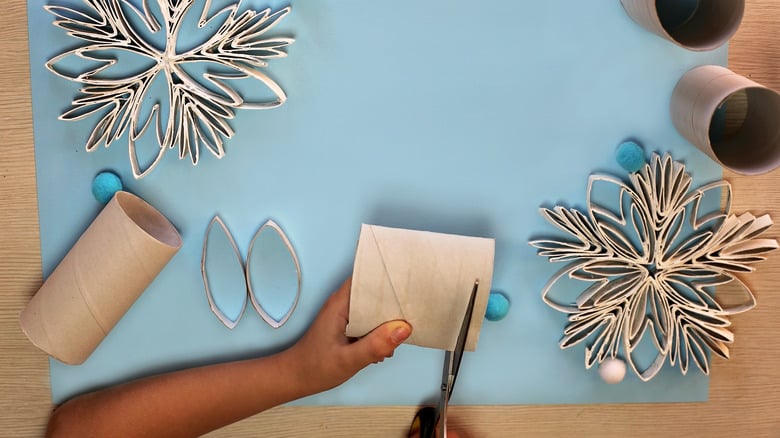 ChristmasCraftedSnowflakesWithPaperToiletteRollLaysOnThe Child crafting snowflakes from toilet paper rolls on a light blue background, using scissors and creating creative winter decorations. | Sky Rye Design Child crafting snowflakes from toilet paper rolls on a light blue background, using scissors and creating creative winter decorations.