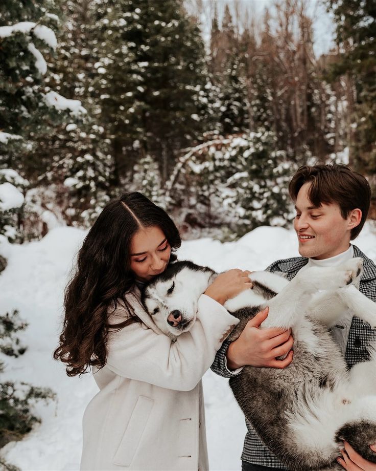lets go play in the snow A couple lovingly hold a husky in a snowy winter forest scene, surrounded by pine trees. | Sky Rye Design A couple lovingly hold a husky in a snowy winter forest scene, surrounded by pine trees.
