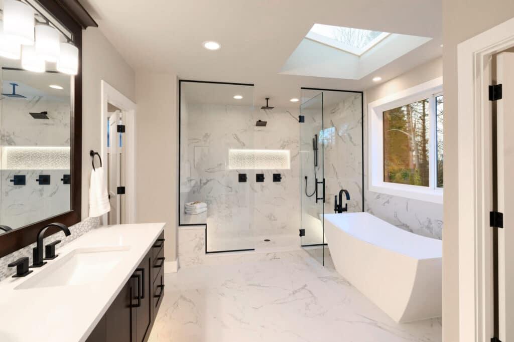 luxury-guest-bath-scaled Modern bathroom with a large glass shower, freestanding tub, double sink, and marble walls, illuminated by a skylight. | Sky Rye Design Modern bathroom with a large glass shower, freestanding tub, double sink, and marble walls, illuminated by a skylight.