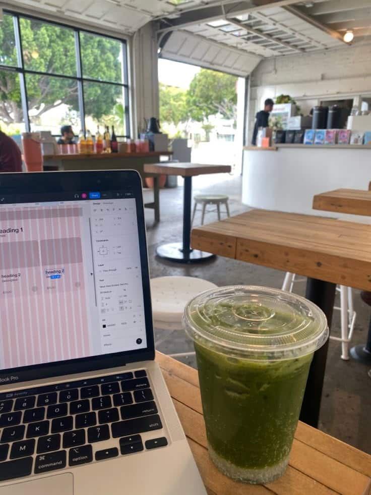 matcha figma Laptop with design software and green juice on a wooden table in a bright, modern cafe setting. | Sky Rye Design Laptop with design software and green juice on a wooden table in a bright, modern cafe setting.