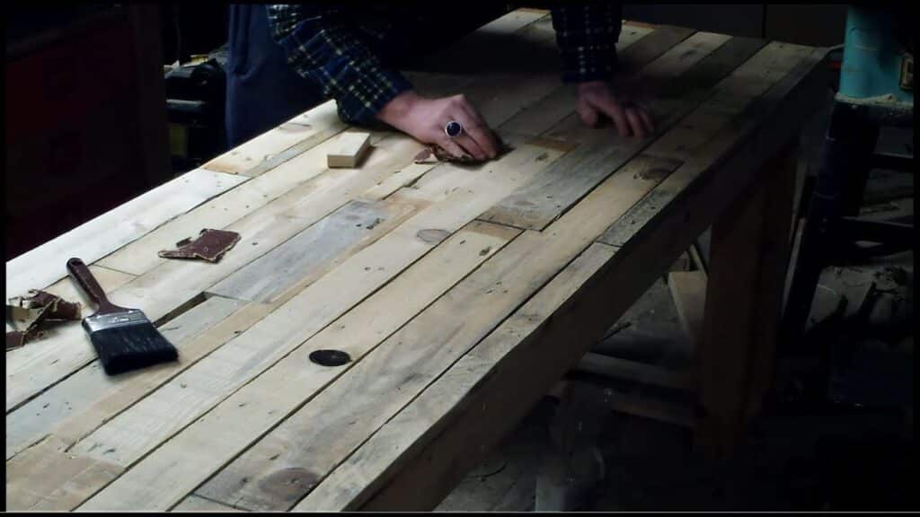 maxresdefault 22 Person sanding a wooden workbench with sandpaper, surrounded by tools and woodworking materials in a dimly lit workshop. | Sky Rye Design Person sanding a wooden workbench with sandpaper, surrounded by tools and woodworking materials in a dimly lit workshop.