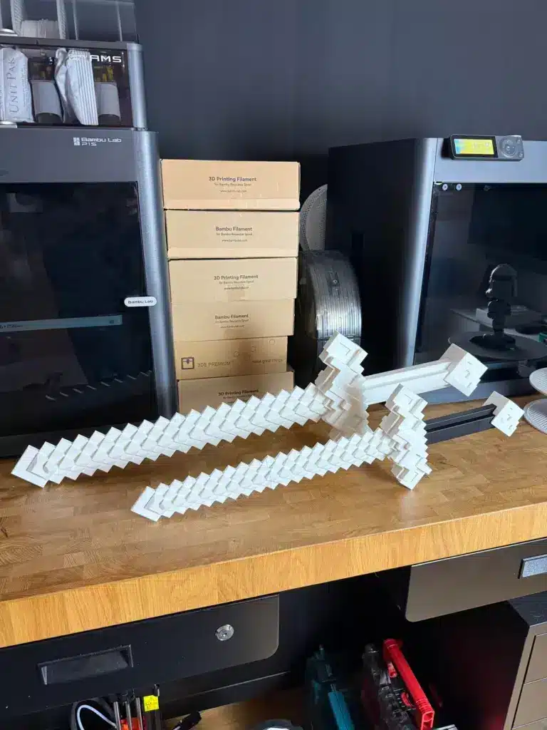 minecraft-swords-crafted-v0-o4bo1yw06yye1 3D printed pixel-style swords on a wooden table, with 3D printers and filament boxes in the background. | Sky Rye Design 3D printed pixel-style swords on a wooden table, with 3D printers and filament boxes in the background.