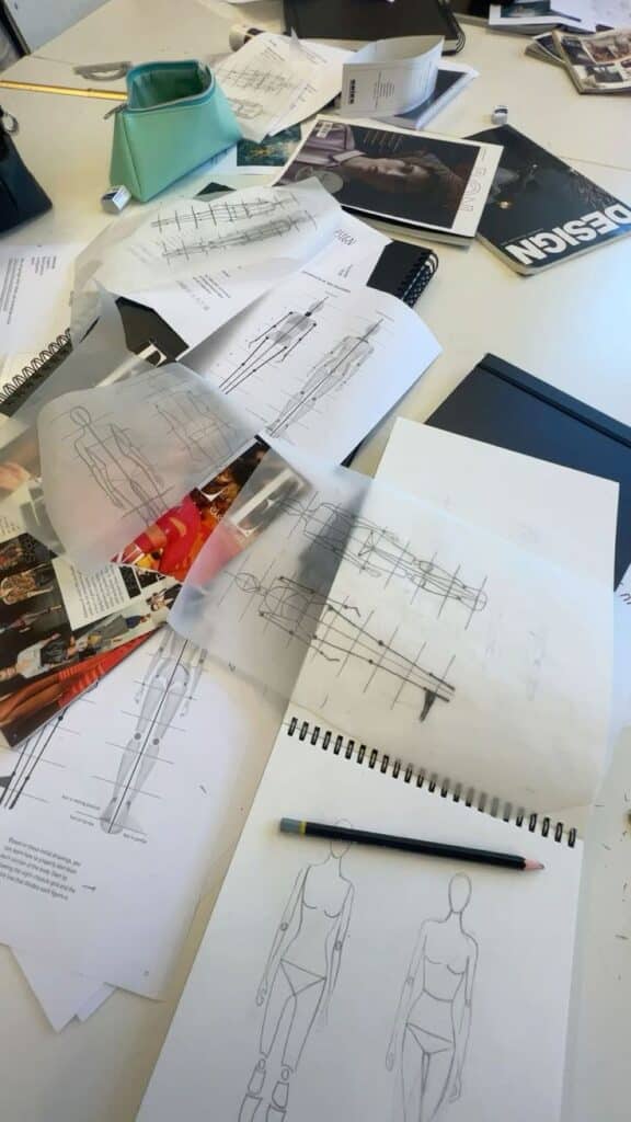 modedesign Design workspace with fashion sketches and magazines on a table, depicting creative process in fashion design studios. | Sky Rye Design Design workspace with fashion sketches and magazines on a table, depicting creative process in fashion design studios. industrial design graduate programs