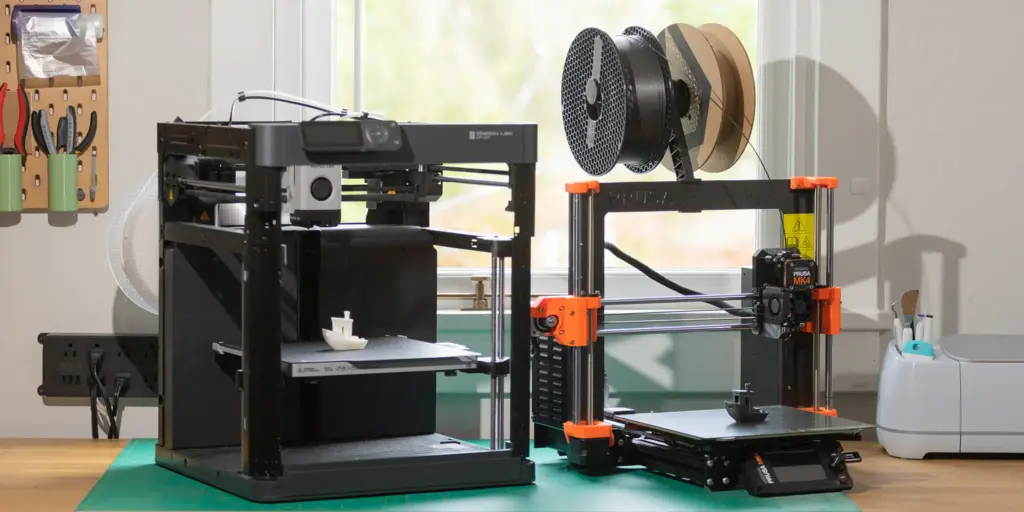 Two 3D printers on a workbench near a window, with a wall-mounted tool organizer and filament spools, ready for printing projects.