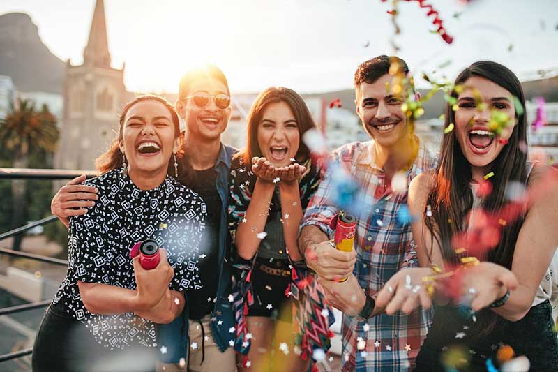 Group of friends joyfully celebrating outdoors with confetti and party poppers, capturing happiness and togetherness in a vibrant setting.