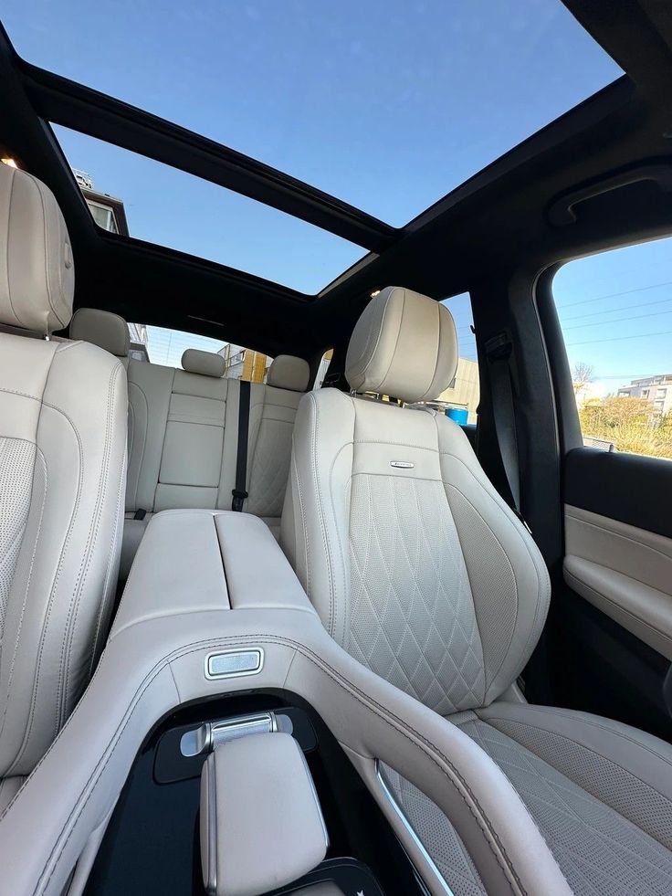 Luxury car interior with beige leather seats, panoramic sunroof, and stylish center console against a clear blue sky backdrop.