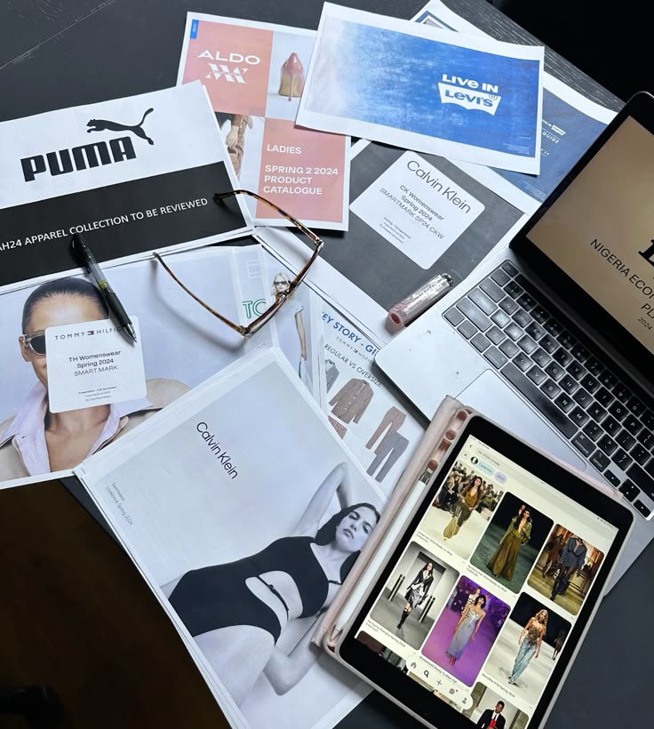 pov you work in fashion Fashion brand strategy meeting with Puma, Levi's, and Calvin Klein catalogs on a desk with laptop and tablet, showcasing design ideas. | Sky Rye Design Fashion brand strategy meeting with Puma, Levi's, and Calvin Klein catalogs on a desk with laptop and tablet, showcasing design ideas.