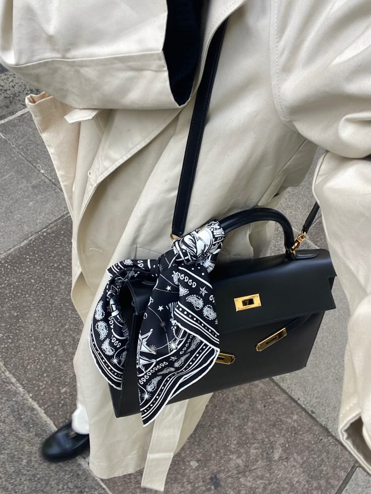 Stylish black handbag with a patterned black and white scarf, paired with a beige trench coat, creating a chic street fashion look.
