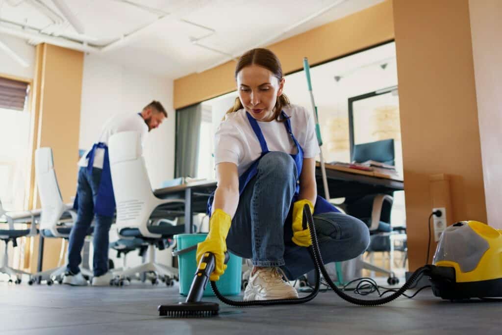 Office cleaning service professionals using vacuum and mop in modern workspace.