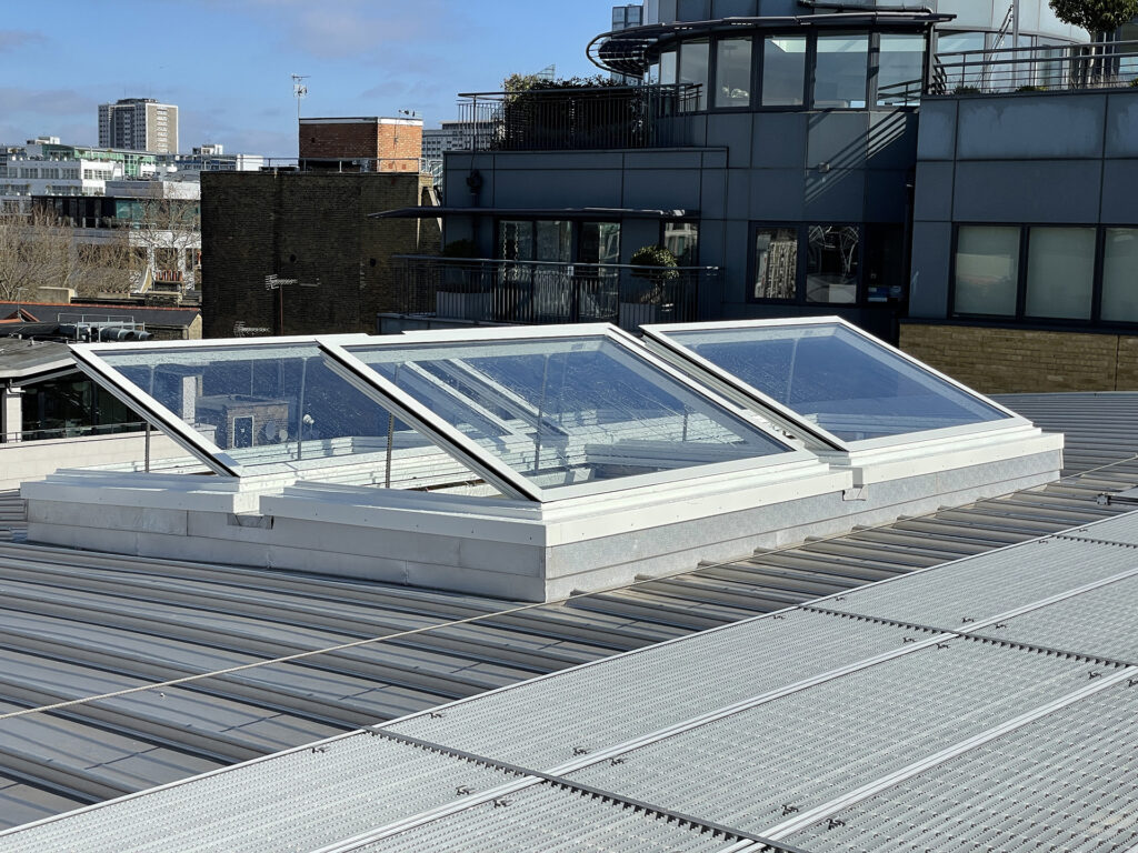 Modern roof with three open skylights, providing natural light to the building interior, set against an urban cityscape background.