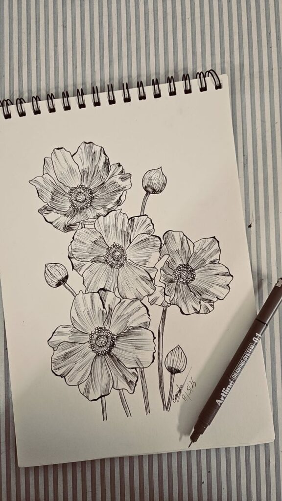 Black ink floral drawing on sketchbook, showcasing detailed poppy flowers with a drawing pen on a striped background.
