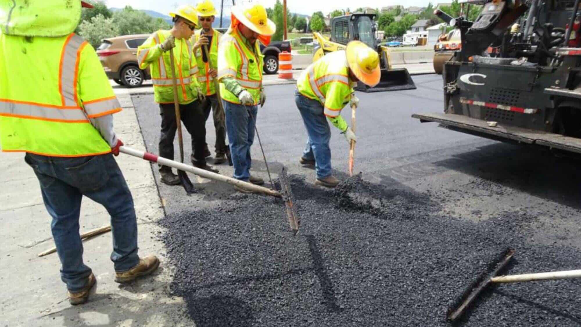 Road construction workers in safety gear spreading asphalt on a street for paving, improving infrastructure and transportation.