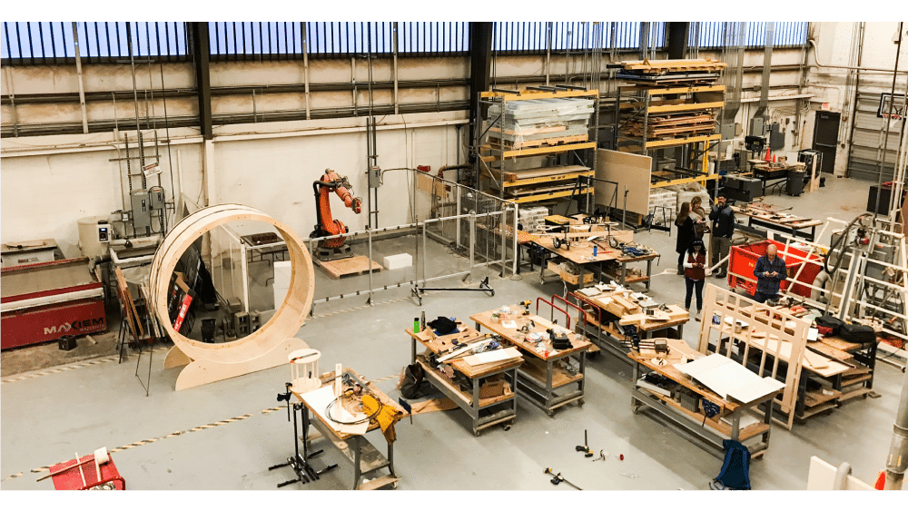 top-student-life-studio-culture-digital-fabrication Spacious industrial workshop with workbenches, robotic arm, and large wooden structure, ideal for engineering and innovation projects. | Sky Rye Design Spacious industrial workshop with workbenches, robotic arm, and large wooden structure, ideal for engineering and innovation projects.