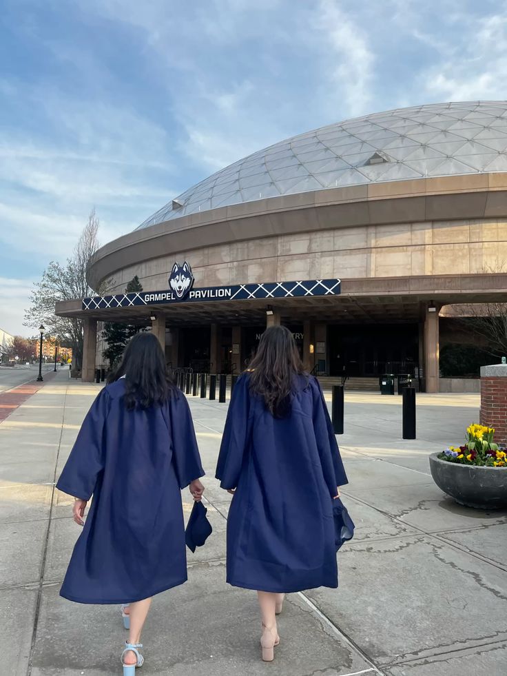 uconn graduation photos Two graduates in blue gowns walk towards Gampel Pavilion under a blue sky, celebrating their achievement. | Sky Rye Design Two graduates in blue gowns walk towards Gampel Pavilion under a blue sky, celebrating their achievement.