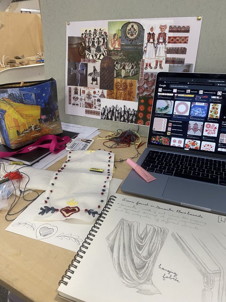 _ Creative workspace with embroidery, sketches, and cultural mood board. Laptop displays traditional textile patterns. Art supplies scattered. | Sky Rye Design Creative workspace with embroidery, sketches, and cultural mood board. Laptop displays traditional textile patterns. Art supplies scattered.