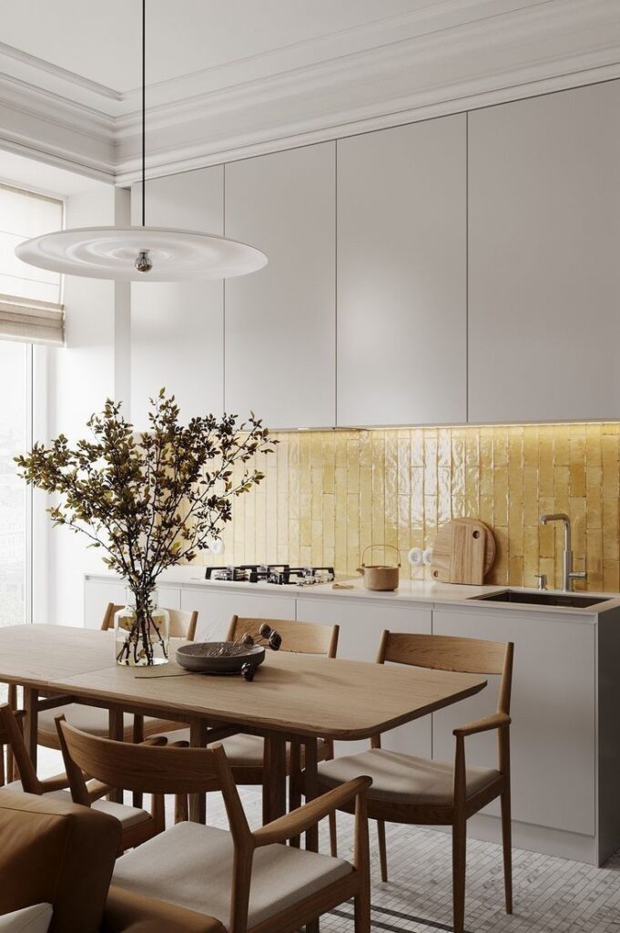 Modern kitchen with light wood dining table, elegant chandelier, yellow tile backsplash, and minimalist white cabinets. Cozy and stylish design.