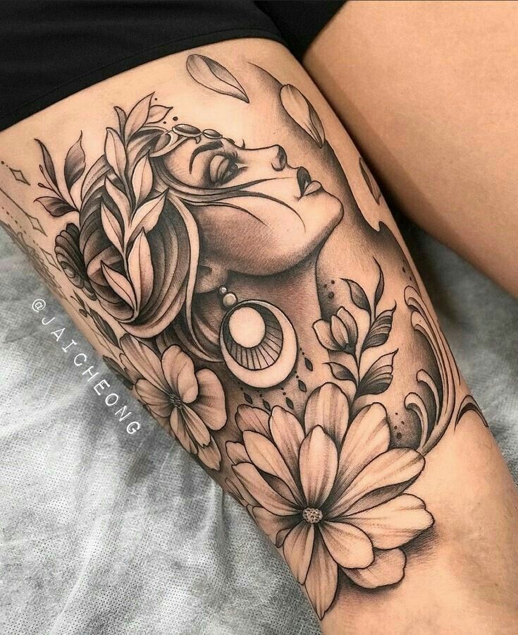 _ Detailed black and gray floral tattoo on thigh, featuring a woman's face with earrings and flowers, surrounded by leaves and petals. | Sky Rye Design Detailed black and gray floral tattoo on thigh, featuring a woman's face with earrings and flowers, surrounded by leaves and petals.