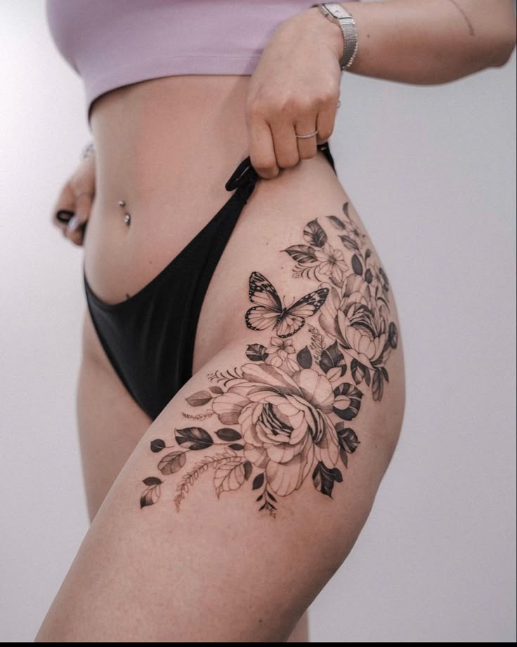 _ Woman showing a detailed floral and butterfly tattoo on her thigh, wearing black underwear and a cropped top, highlighting body art. | Sky Rye Design Woman showing a detailed floral and butterfly tattoo on her thigh, wearing black underwear and a cropped top, highlighting body art.