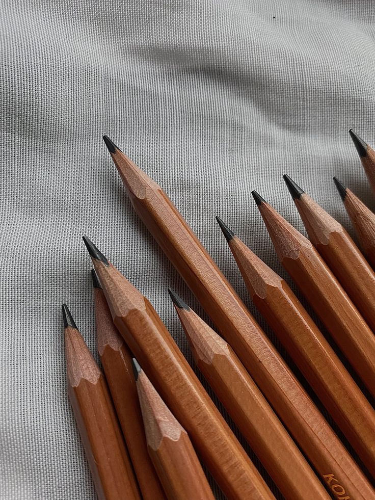 Sharpened wooden pencils arranged in a row on a gray textured fabric background. Ideal for artists, students, and writing enthusiasts.