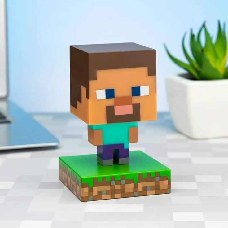 _ Block-style character figurine from a popular game on a desk, with a laptop and potted plant in the background. | Sky Rye Design Block-style character figurine from a popular game on a desk, with a laptop and potted plant in the background.
