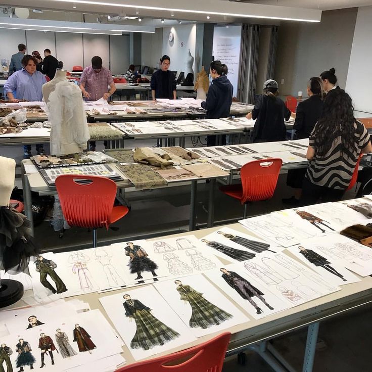 Fashion design students working in a studio, with sketches and fabric samples on tables, focusing on innovative clothing concepts.