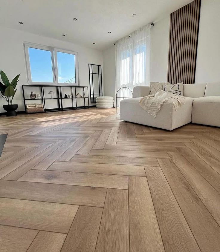 Modern living room with natural light, herringbone wooden floor, white sofa, and minimalist decor.