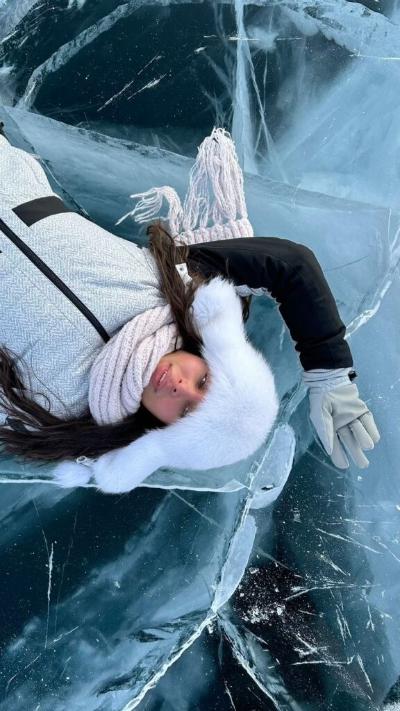 Байкал Лед эстетика зима Woman in winter clothing lying on clear, cracked ice, wearing a white fur hat and scarf, showcasing winter fashion outdoors. | Sky Rye Design Woman in winter clothing lying on clear, cracked ice, wearing a white fur hat and scarf, showcasing winter fashion outdoors.