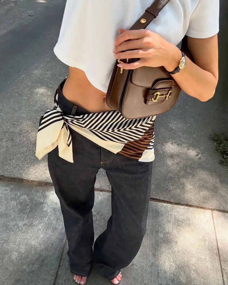 Fashionable outfit with a scarf belt, brown bag, white crop top, and jeans.