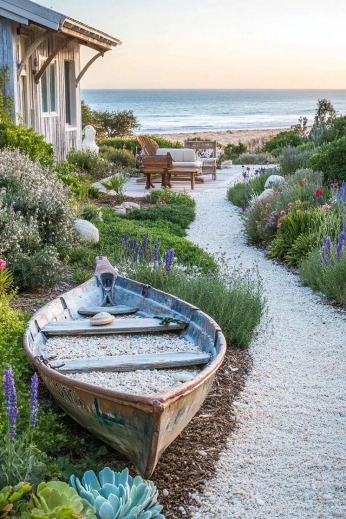 Coastal garden with a path leading to a beachside deck, featuring an old boat filled with pebbles and surrounded by colorful plants.
