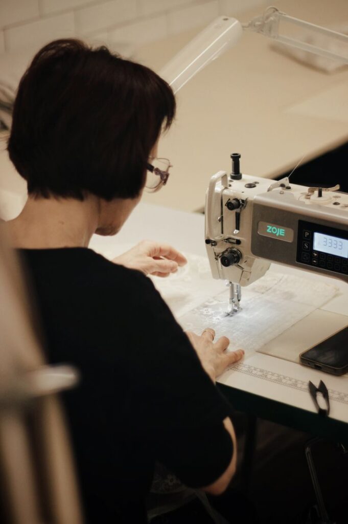 Производство тюля в цехе Decortier Person sewing fabric with a Zoje industrial machine, focused on intricate stitching in a well-lit workspace. | Sky Rye Design Person sewing fabric with a Zoje industrial machine, focused on intricate stitching in a well-lit workspace.