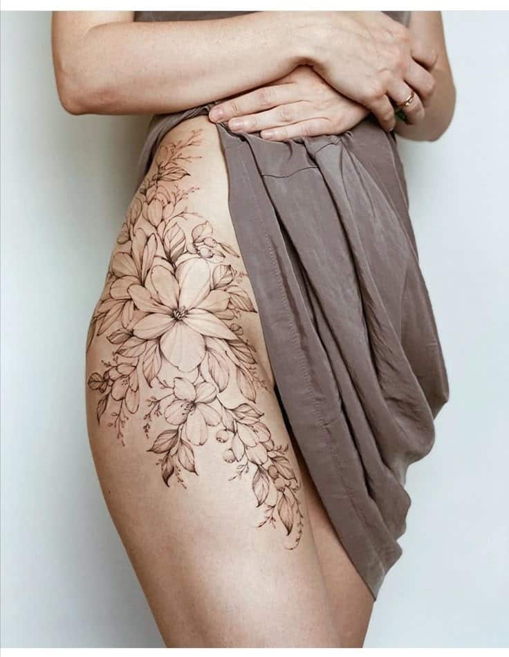 Тату на бедре Floral tattoo design on a woman's thigh, adorned with intricate blossoms, partially covered by a draped skirt. | Sky Rye Design Floral tattoo design on a woman's thigh, adorned with intricate blossoms, partially covered by a draped skirt.