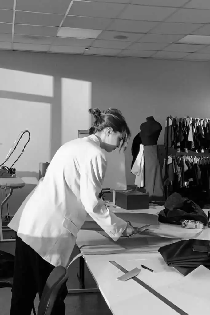 Французский институт моды ModArt Designer working in a fashion studio, cutting fabric on a table with mannequins and textiles in the background. | Sky Rye Design Designer working in a fashion studio, cutting fabric on a table with mannequins and textiles in the background.
