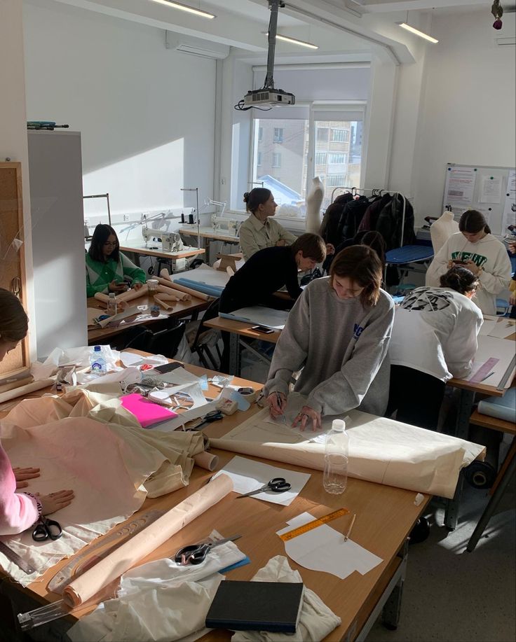 мастерская Design students working on clothing patterns in a sunlit classroom, surrounded by fabrics, scissors, and sewing machines. | Sky Rye Design Design students working on clothing patterns in a sunlit classroom, surrounded by fabrics, scissors, and sewing machines.