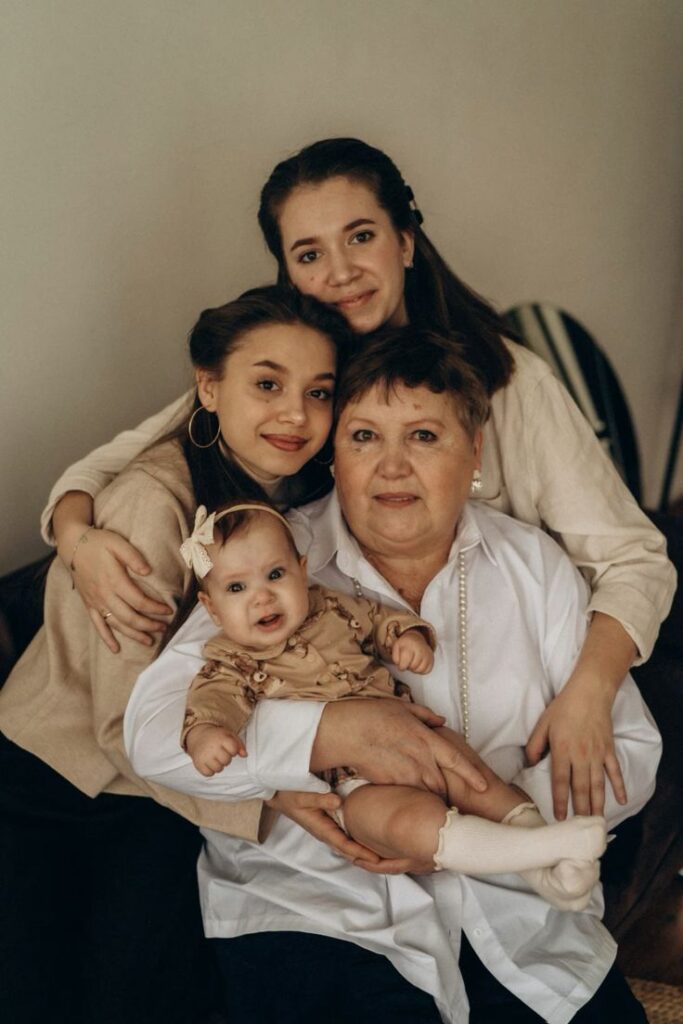 семейныйфотографсемейнаяфотографиястудиялокациядляфотосессиисемейныефотосессиифотографияфотограффотографмосква_ Four generations of women smiling together, showcasing family love and togetherness in a warm, cozy setting. | Sky Rye Design Four generations of women smiling together, showcasing family love and togetherness in a warm, cozy setting.
