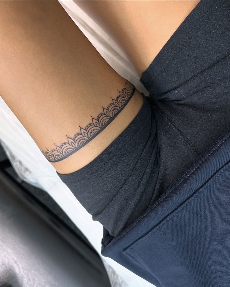 тату татуировка татубраслет tattoo Ornate lace tattoo encircles an upper thigh, showcasing intricate design on tan skin, partially covered by black shorts. | Sky Rye Design Ornate lace tattoo encircles an upper thigh, showcasing intricate design on tan skin, partially covered by black shorts.