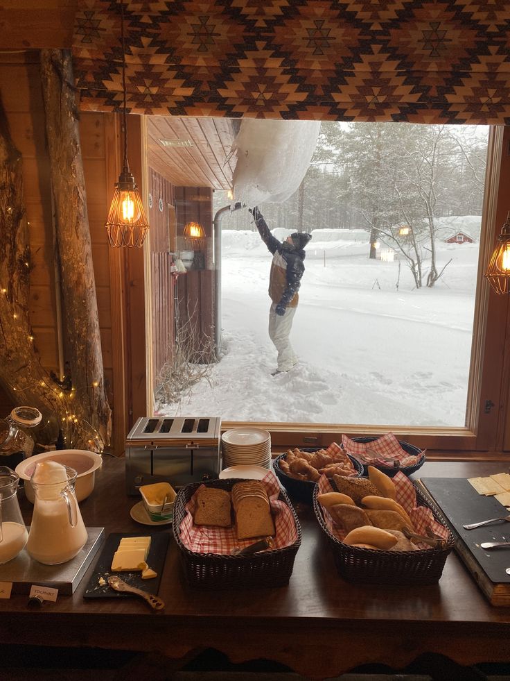 Cozy cabin breakfast with bread and milk, while snow falls outside and person interacts with icicles, creating a serene winter scene.