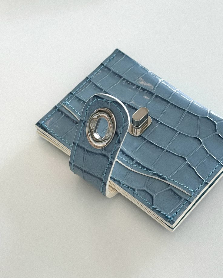 Blue textured leather wallet with a metal clasp on a light background, showcasing a sleek and modern design suitable for everyday use.