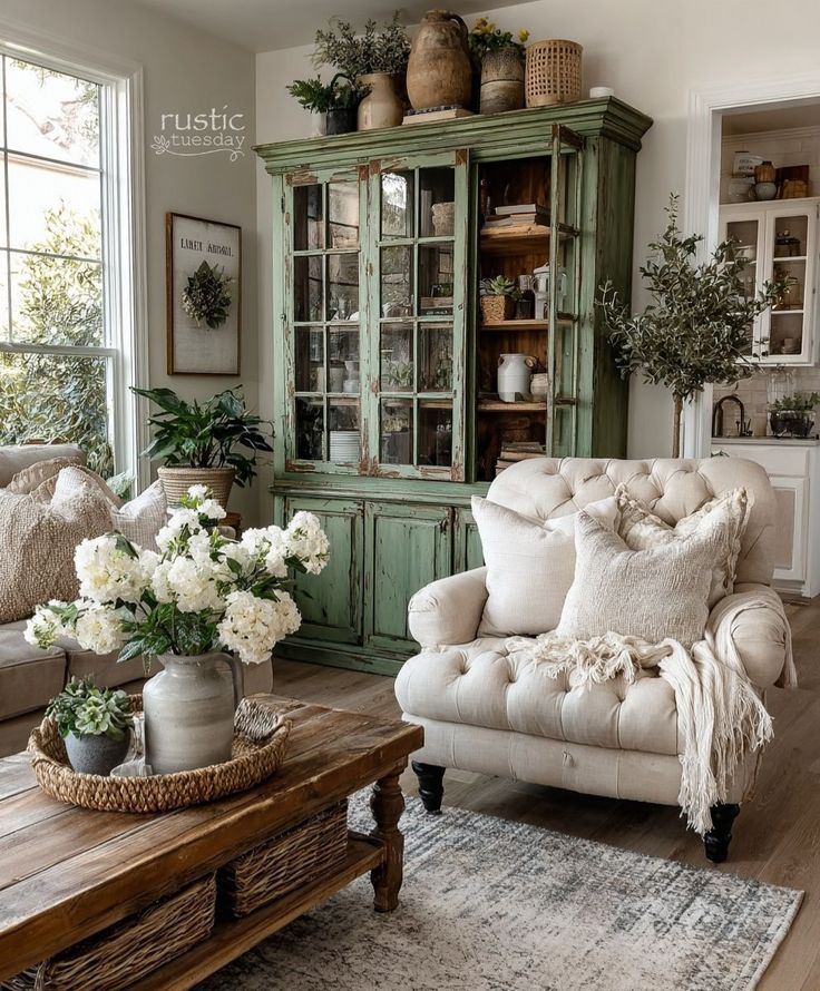 𝚛𝚞𝚜𝚝𝚒𝚌 - The kind of room that feels like a deep breath layers of texture softness and timeworn grace_ 🤍🌿 𓅪𓅪𓅪 RusticTuesday GreenCabinet FarmhouseLivingRoom CollectedAndCozy CottageStyleDecor Vin Cozy rustic living room with vintage green cabinet, tufted armchair, wooden coffee table, white flowers, and homey decor elements. | Sky Rye Design Cozy rustic living room with vintage green cabinet, tufted armchair, wooden coffee table, white flowers, and homey decor elements.