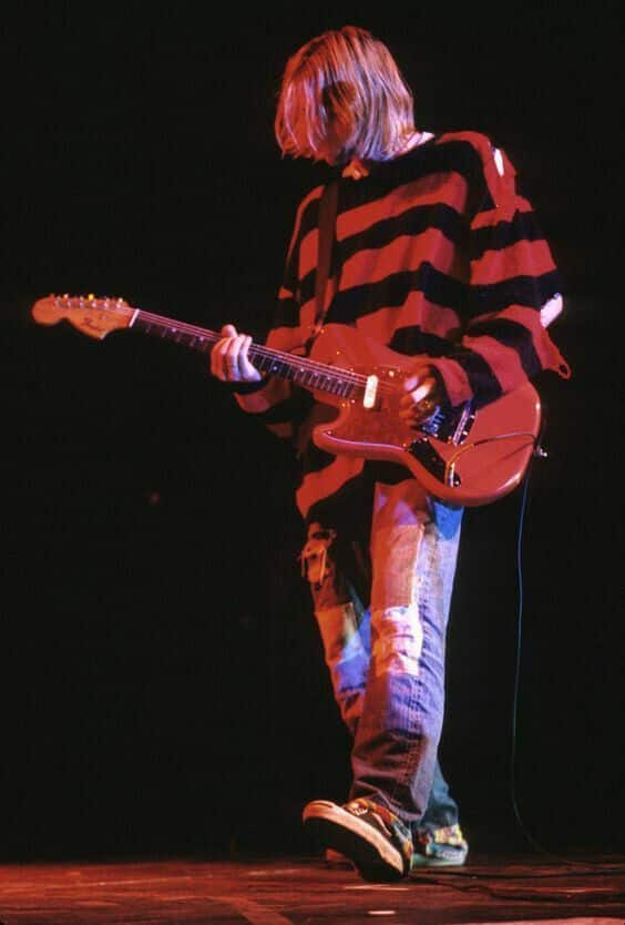 Musician in striped sweater playing electric guitar on stage, exuding grunge style. Vintage vibes with a powerful performance.