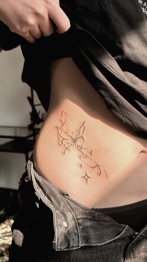 тату бабочки Delicate butterfly tattoo design on side torso, surrounded by stars and swirls, with person pulling up shirt to reveal artwork. | Sky Rye Design Delicate butterfly tattoo design on side torso, surrounded by stars and swirls, with person pulling up shirt to reveal artwork.