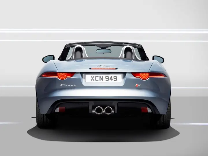 Rear view of a sleek silver sports car with dual exhausts and a convertible top, emphasizing modern design and luxury performance.