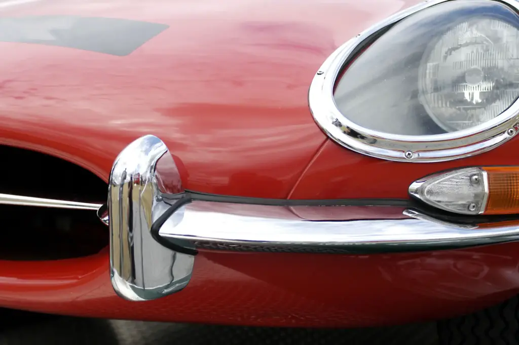 Close-up of a classic red car with chrome bumper and round headlight, highlighting vintage automotive design details.